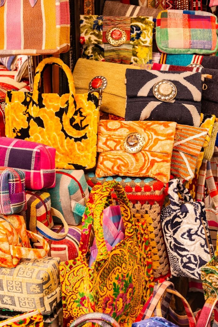 Vibrant collection of handmade handbags on display at a market, showcasing colorful patterns and textures.